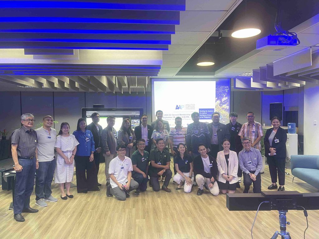 Group photo of new members of the Analytics and AI Association of the Philippines standing and kneeling in front of a screen displaying the AAP logo
