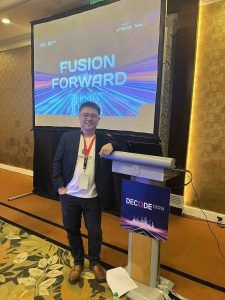 Allan Tan standing beside a lectern in front of a large screen displaying the DECODE 2024 'FUSION FORWARD' title slide
