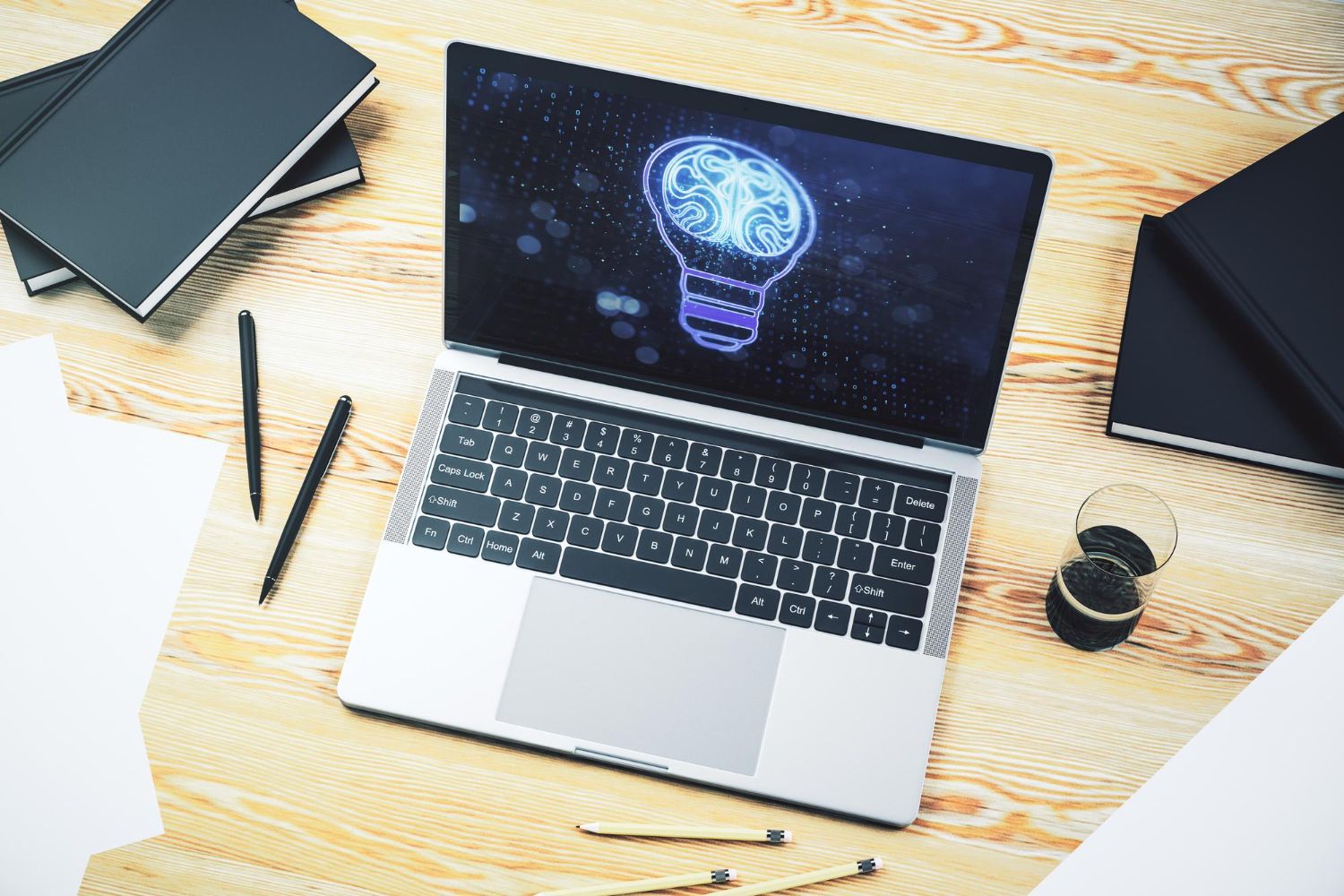 Stock photo of a laptop on a desk displaying a glowing digital brain inside a light bulb outline, symbolizing AI-generated ideas