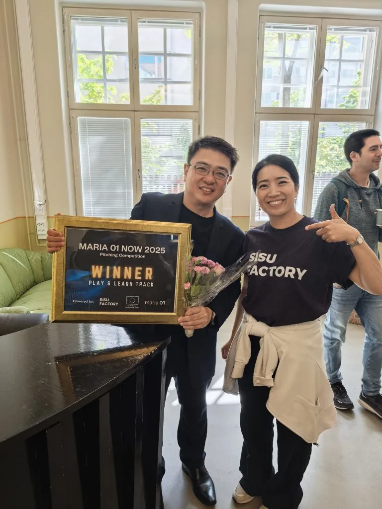 PSI representative posing with a Sisu Factory team member, both smiling, while he holds the framed Maria 01 NOW 2025 winner certificate and flowers