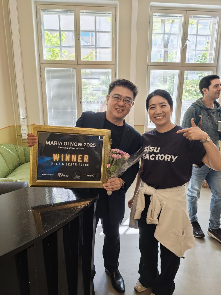 PSI representative posing with a Sisu Factory team member, both smiling, while he holds the framed Maria 01 NOW 2025 winner certificate and flowers