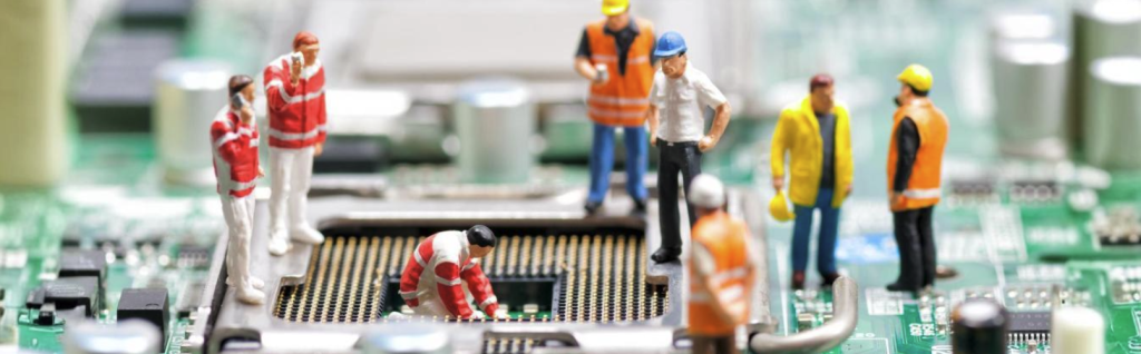 Stock photo of miniature figurines in work overalls and hard hats appearing to service a computer circuit board, illustrating small-scale AI models