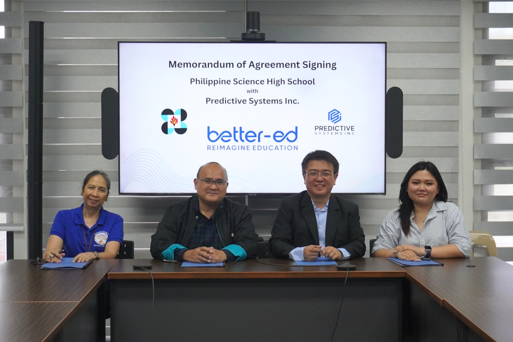 The same four signatories now smiling at the camera after signing, seated behind the MOA signing screen showing the PSHS, better-ed, and Predictive Systems Inc. logos